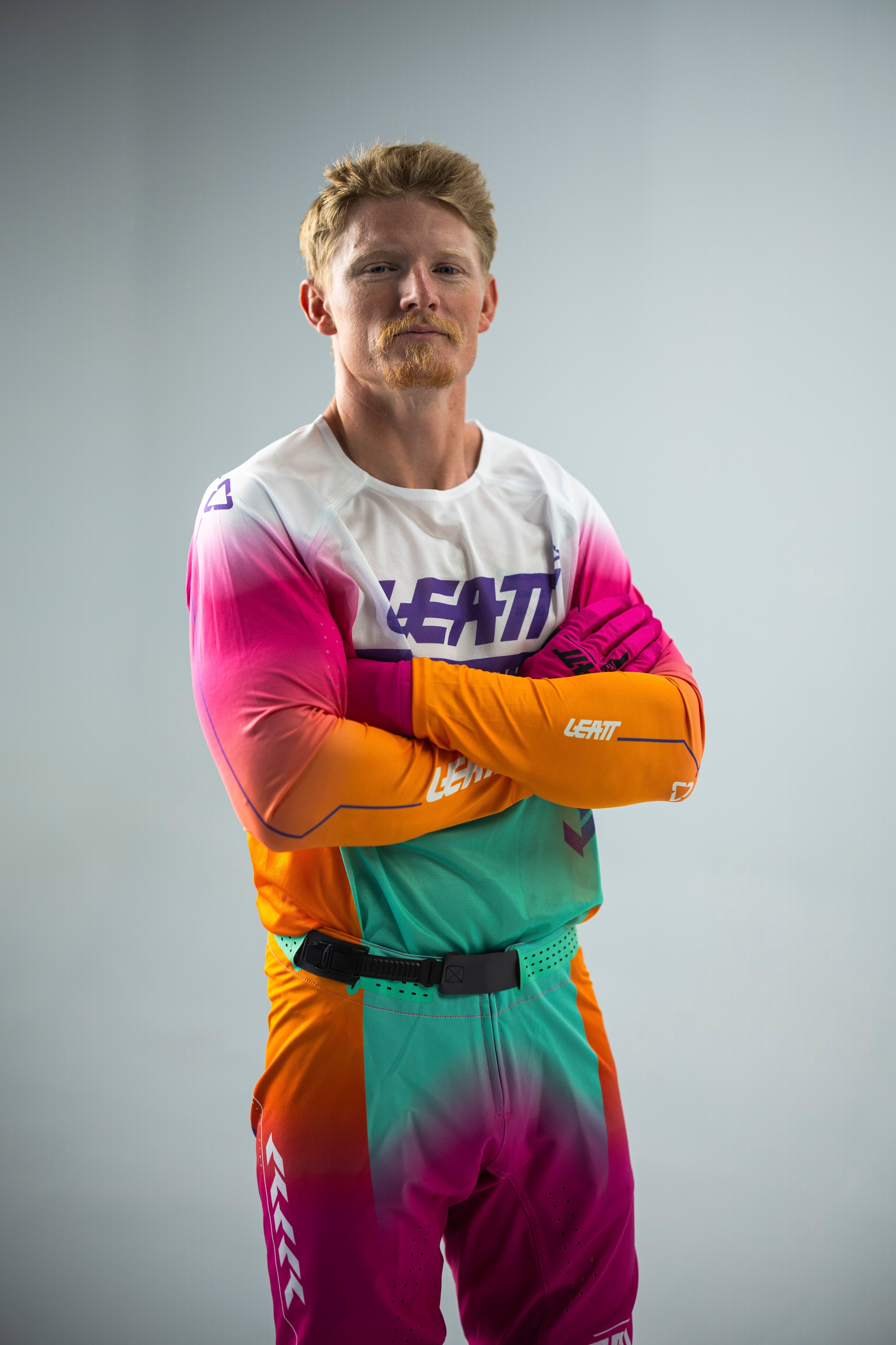 Justin Hill wearing a colorful Leatt racing suit on a gray background